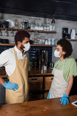 African american baristas in medical masks and latex gloves talking in cafe