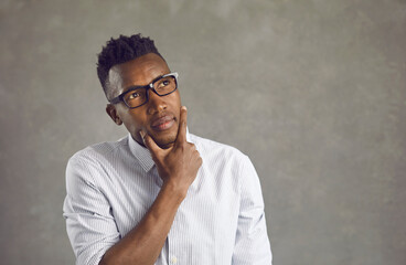 Black man in white office shirt and eyeglasses looks up thinking, wondering, taking decision. African American business manager with thoughtful face expression unsure, doubting, uncertain, hesitating