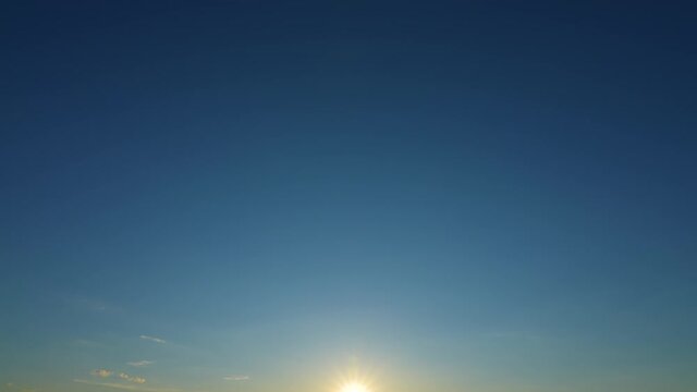 Sunset time and clear blue sky with some white fluffy clouds and sun shining softly. Video time lapse of peaceful evening clear blue sky and sun star sparkling in bottom of frame