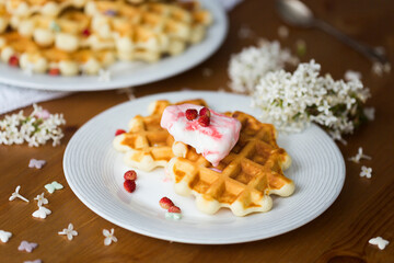 Homemade viennese waffles with fresh strawberries and ice cream on white plates on white tablecloth and white lilac branches and flowers on wooden table