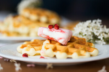 Homemade viennese waffles with fresh strawberries and ice cream on white plates on white tablecloth and white lilac branches and flowers on wooden table