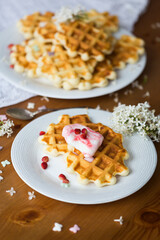 Homemade viennese waffles with fresh strawberries and ice cream on white plates on white tablecloth and white lilac branches and flowers on wooden table