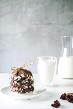 Front view of freshly baked chocolate cookies and glass of milk on rustic wooden table over gray background. Copy space. Vertical image.