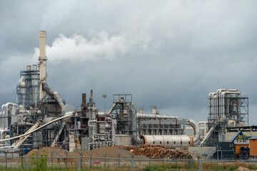 Wood processing plant against the background of gray clouds. White toxic smoke comes out of factory chimneys. Utopian landscape. Environmental pollution. An environmental disaster.