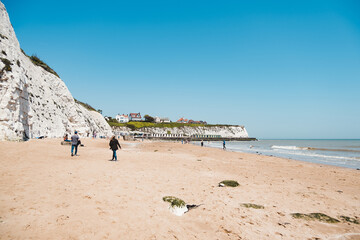 People chilling at Dumpton Gap bay with colourful wooden beach huts between Broadstairs and Ramsgate