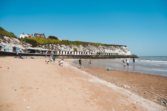 People chilling at Dumpton Gap bay with colourful wooden beach huts between Broadstairs and Ramsgate
