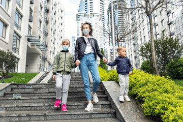 Fototapeta na wymiar Young adult caucasian mother walking downstairs together with son and daughter children in city center downtown against building. New normal urban people lifestyle post coronavirus life. Candid