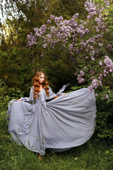 Fototapeta premium Girl in long dress near lilac on green summer background