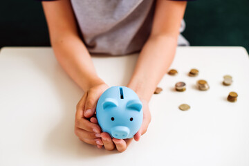 Teen boy holding blue piggy bank. Kids financial education and responsibility, accumulation and savings planning. The child manages and deposits his finance, Investment concept.