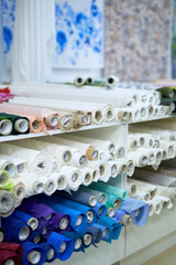 Colorful textile rolls in blue, pink, green, red, white colors in textile store or warehouse lying on a shelves. Fabrics retail store, drapery shop or atelier. High quality vertical image