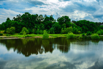 Fototapeta na wymiar forest mirroring the lake with cloudy skies