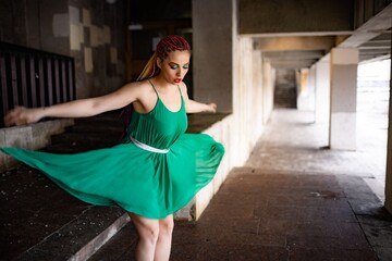 A girl with bright braids and glitter colored makeup in a bright green spring dress jumps off the steps of an old building