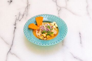 Mixed sea bass and prawn ceviche with marinated sweet potato and corn on a blue deep plate