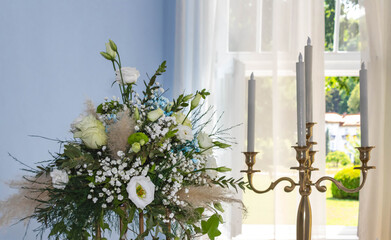 A bouquet of flowers and a candlestick in front of a curtain and an open window in daylight, romantic and elegant