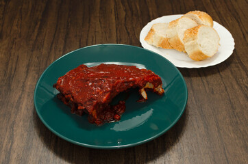 Roasted ribs with barbecue sauce served in a green plate on a wooden plate.