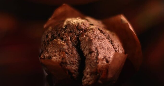 Dark brown chocolate muffin rotating in a dark background. Close up view filmed with RED camera.