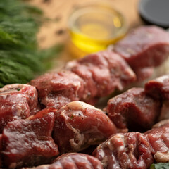 Raw meat is marinated for baking on skewers. Kebab preparatory and cooking Process. Sirloin, spices and greens on kitchen table. Blurred background. Close up shot. Soft focus. Square format.