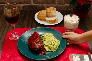 Plate of food on wooden table. Roasted ribs marinated with barbecue sauce, spaghetti and wine. Person's hand interacting with food.