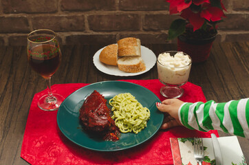 Plate of food on wooden table. Roasted ribs marinated with barbecue sauce, spaghetti and wine. Person's hand interacting with food.