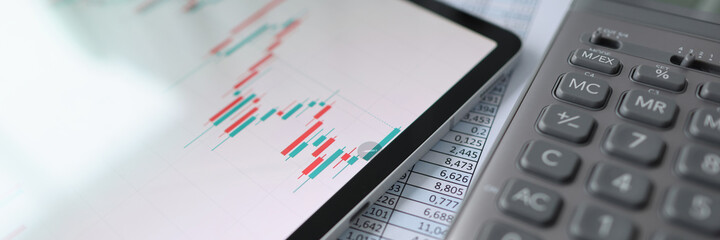 On table is tablet with commercial charts, calculator and documents with reports