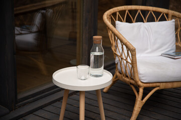 Chair near table with white clean pillow and class of water at the table on terrace in the countryside house.