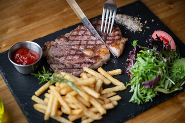 cutting steak with knife and fork on black plate