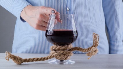 female hand shows the sign CANNOT, STOP on a wine glass, tied with a jute rope. The concept of alcohol addiction. The problem of alcoholism treatment