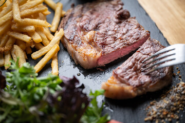 cutting steak with knife and fork on black plate