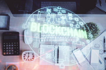 Blockchain theme hologram drawings over computer on the desktop background. Top view. Multi...