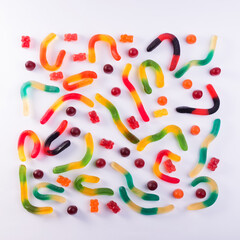 Pattern of colorful gummy bears and worms against white background top view.