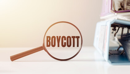 Magnifying glass with the word BOYCOTT on office table.