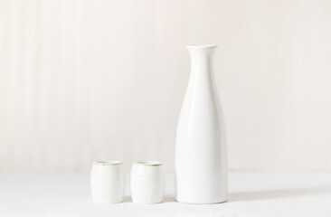 White vase and two white glasses on a white table. In the background is a light milky background.