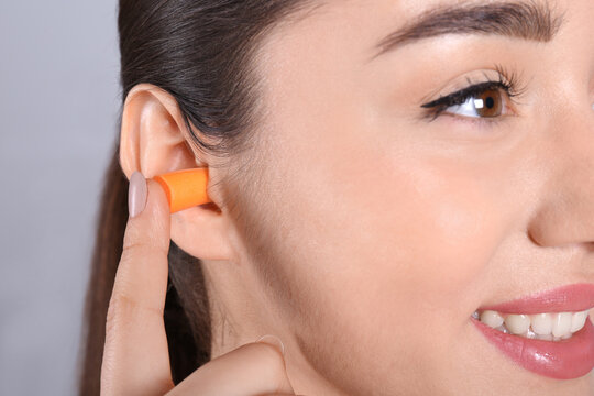 Young Woman Inserting Foam Ear Plug On Grey Background, Closeup