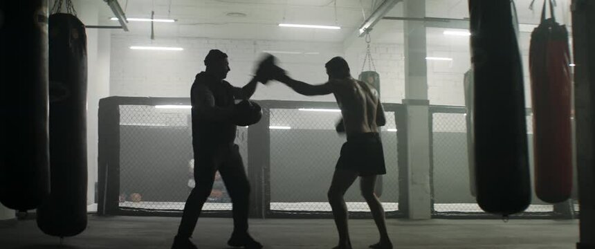WIDE to CU Caucasian male boxer practicing with his trainer in a boxing gym, preparing for a fight. Shot with 2x anamorphic lens