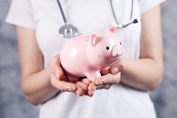 doctor with stethoscope holding a piggy bank