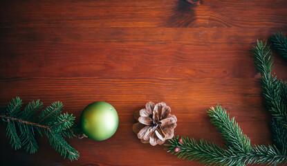 Christmas background, green pine branches with cones and Christmas balls on a brown wooden background. Creative composition with border and copy space, top view. New year, holiday