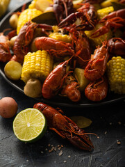 The photo shows a large dish with boiled crayfish and pieces of corn. In the foreground is half a lemon, a large crayfish and potatoes. Close-up.