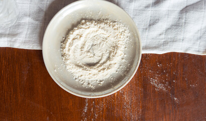 White wheat flour in a plate on a rustic wooden table, top view