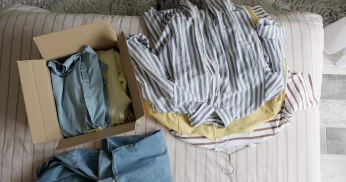 Top view of woman packing used casual clothes into box to sell online as second hand or donation, sustainable living concept.
