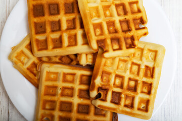 Freshly cooked Belgian waffles on a white plate on a light wooden background.