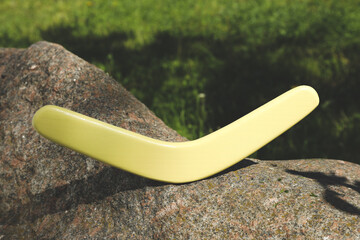 Sunlit yellow wooden boomerang on stone outdoors