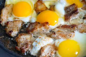 Many eggs with bright yellow yolks and pork lard with meat are fried in a pan. Breakfast or dinner for the whole family. Traditional food of Russians, Belarusians or Ukrainians.