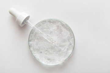 Close-up transparent cosmetic gel in glass petri dish with pipette on white background. Concept...