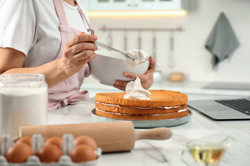 Woman making cake while watching online cooking course via laptop in kitchen, closeup