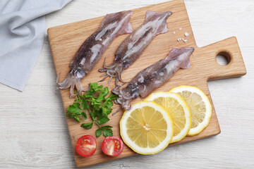 Fresh raw squids with lemon, parsley and tomato on white wooden table, top view