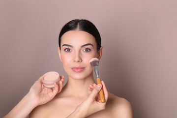 Fototapeta premium Professional makeup artist applying powder onto beautiful young woman's face with brush on dusty rose background