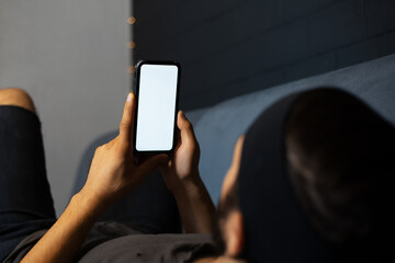 Close-up of young man lying on sofa and using smartphone with mockup.