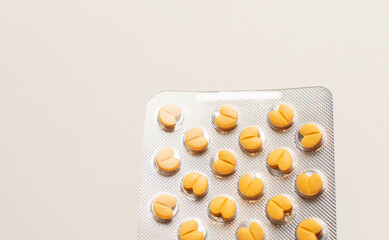 Close-up of blister with pills on pastel yellow background.