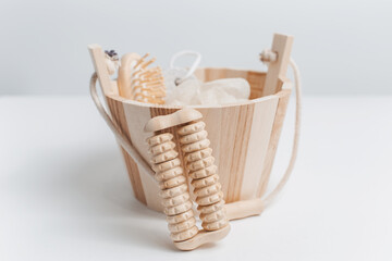 Fototapeta na wymiar Close-up of wooden massager tool near small bucket with other bath accessories against white studio background.