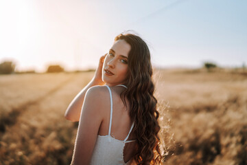 Chica joven atractiva posando en mitad de un campo de trigo al atardecer con tonos dorados